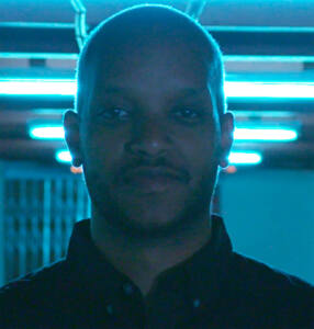 Headshot of Filmmaker Ameha Molla from the shoulders up backlit with blue light
