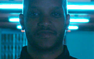 Headshot of Filmmaker Ameha Molla from the shoulders up backlit with blue light